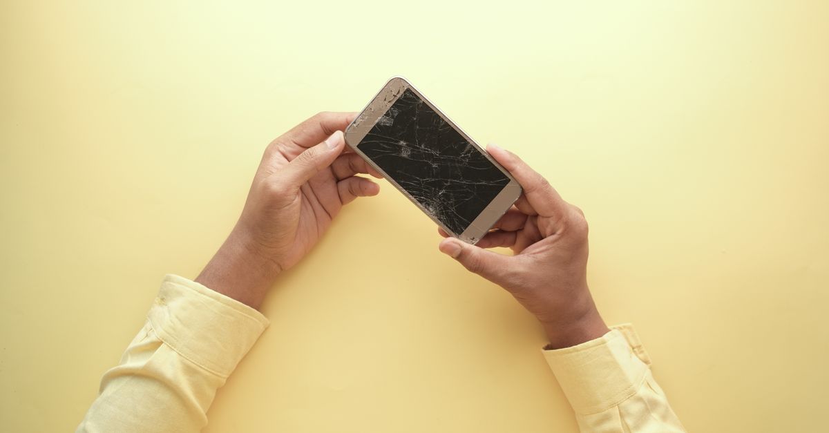 person holding an old iPhone with a cracked screen, smiling, in a cozy minimalist room