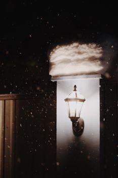 Outdoor wall lamp covered with snow during a winter night snowfall, creating a serene ambiance.