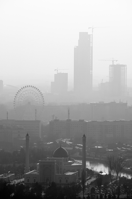 A monochromatic view of Tashkent's skyline features tall buildings and a mosque shrouded in fog.