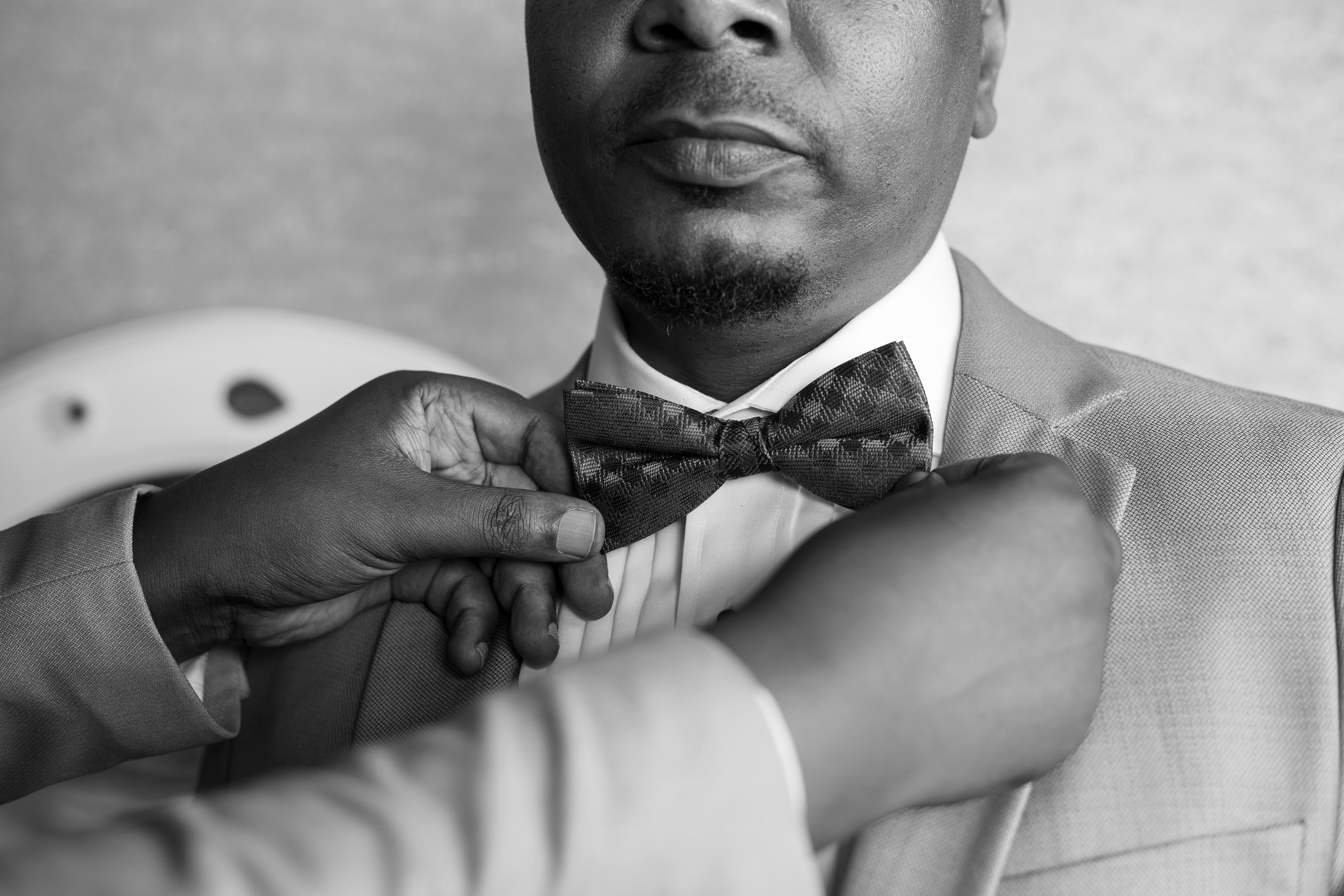 Close-up of a man adjusting a bow tie in a grayscale photo