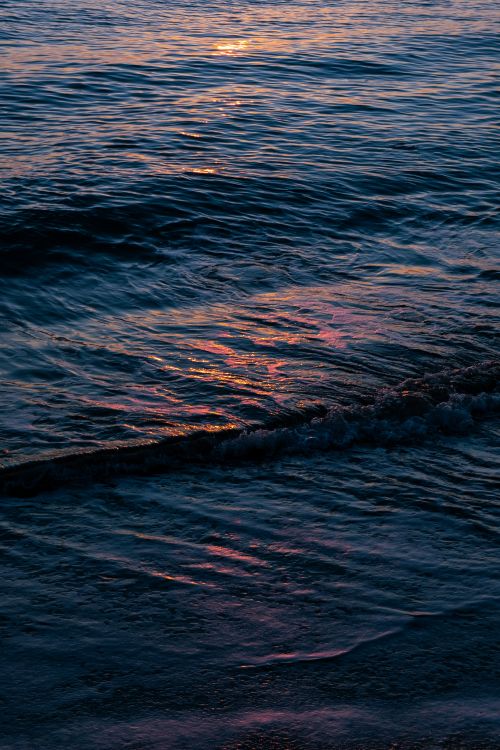 Free Gentle waves at sunset create a serene ocean view with vibrant reflections. Stock Photo