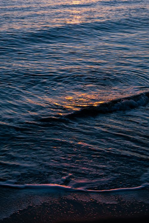 Free Calm waves reflecting the warm sunset glow, creating a serene seascape on a tranquil beach. Stock Photo