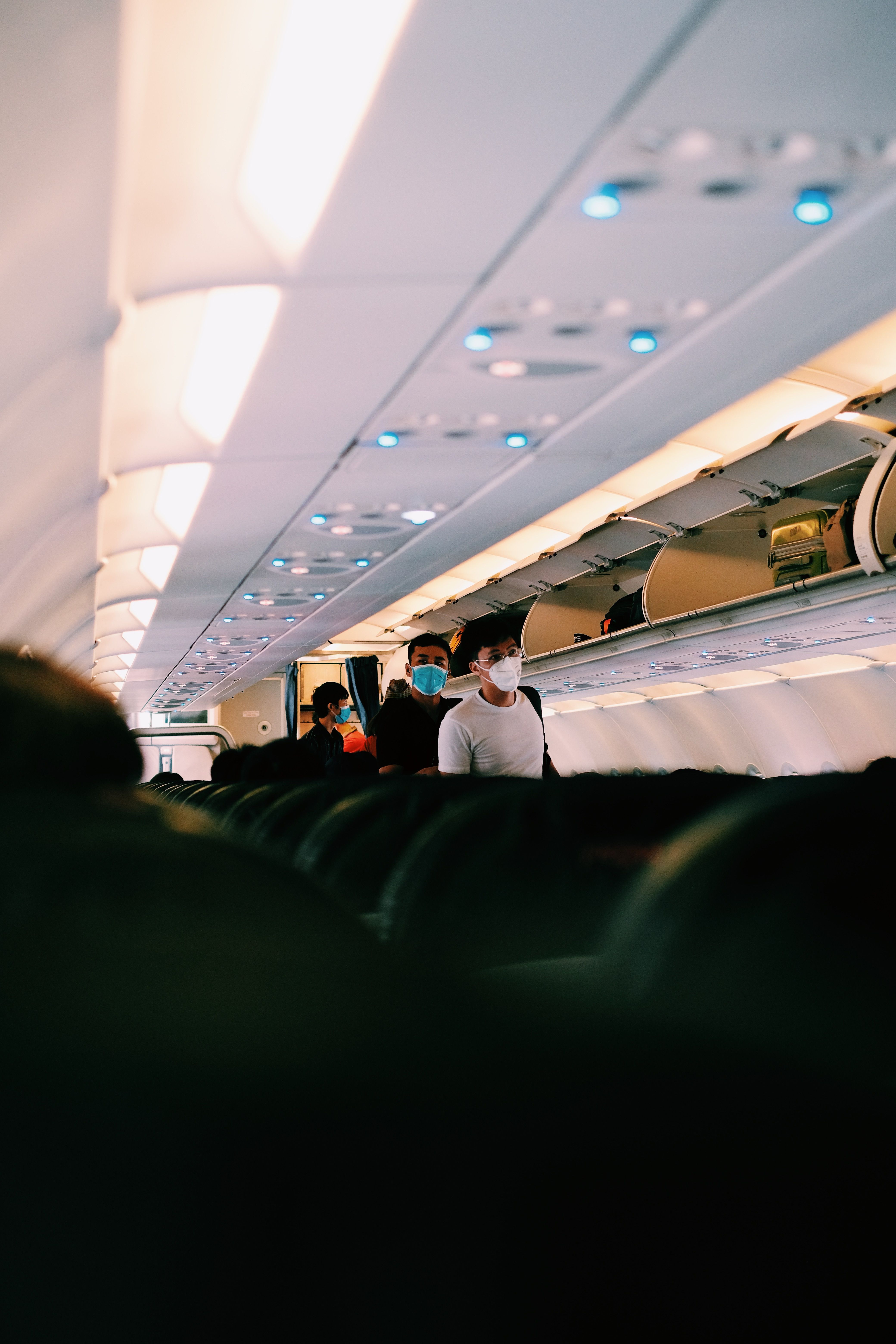 Inside airplane with passengers wearing face masks walking through the aisle.