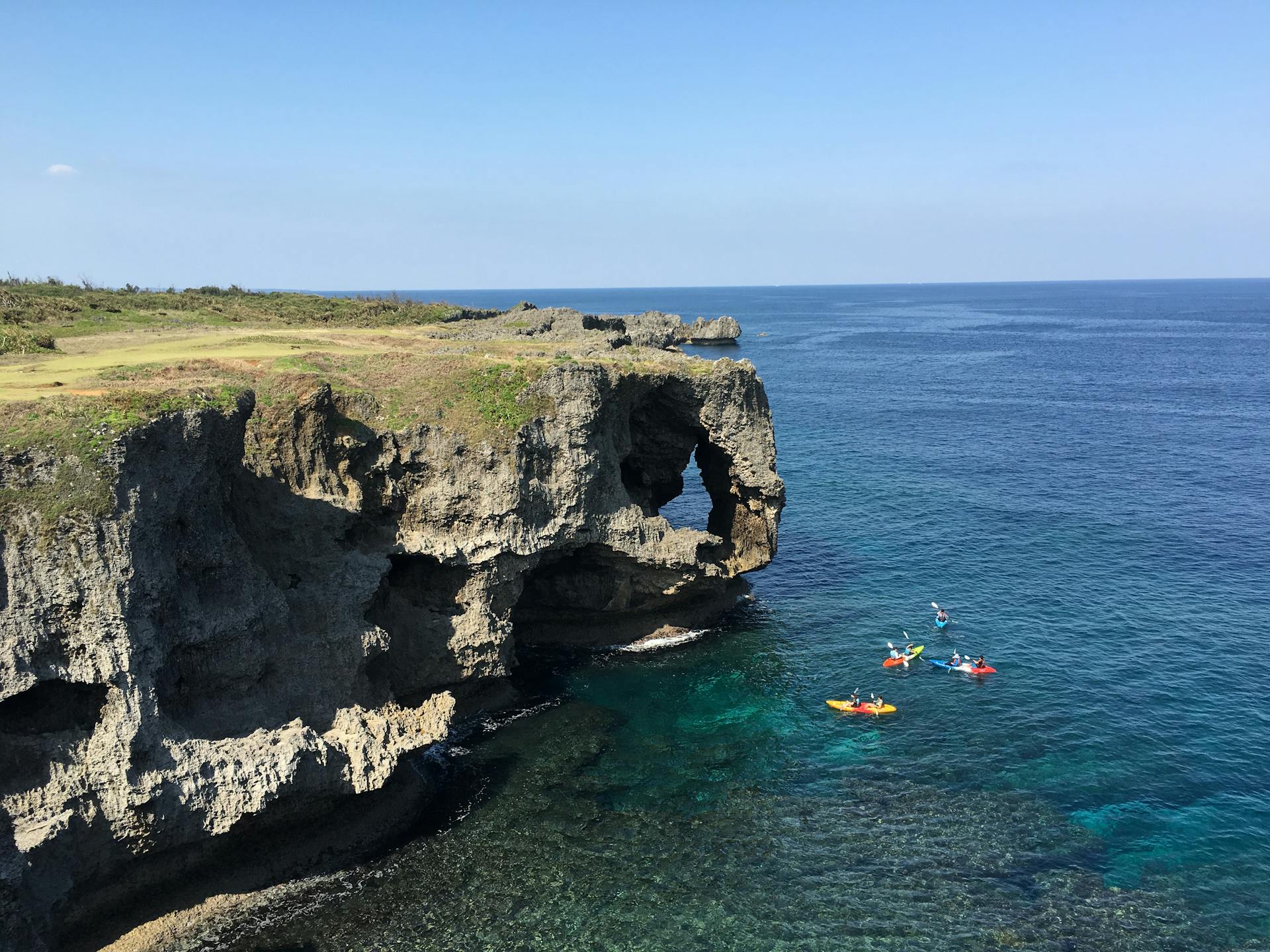 Explore the stunning Cape Manzamo cliffs and clear blue ocean waters in Okinawa, Japan, with kayakers in view.