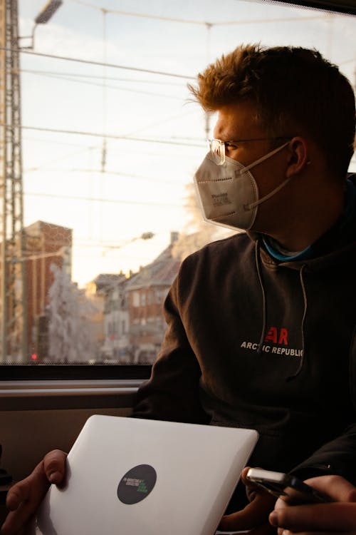  A Man in a Face Mask Sitting by a Glass Window