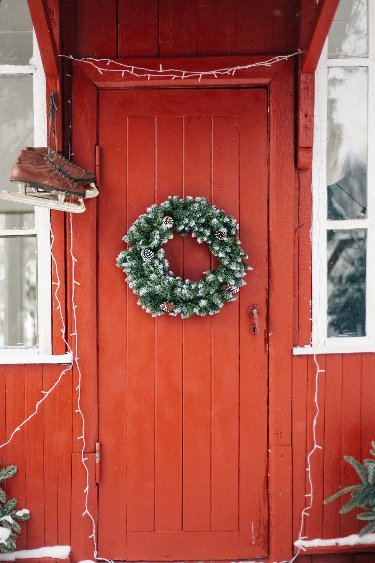 Cozy red wooden door with a green wreath and ice skates for Christmas entryway decor