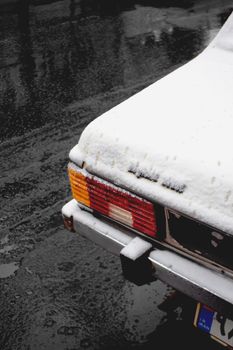 Image of a snow-covered car parked on a wet winter road in Tehran, Iran.