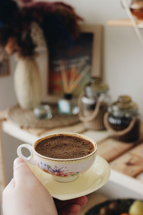 Free A close-up of a hand holding a vintage ceramic cup filled with frothy Turkish coffee indoors. Stock Photo