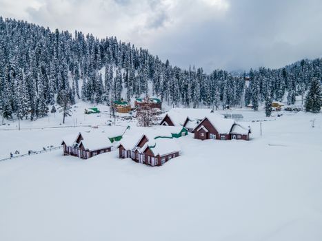 A serene winter landscape featuring quaint cottages blanketed in snow, nestled in a forest.