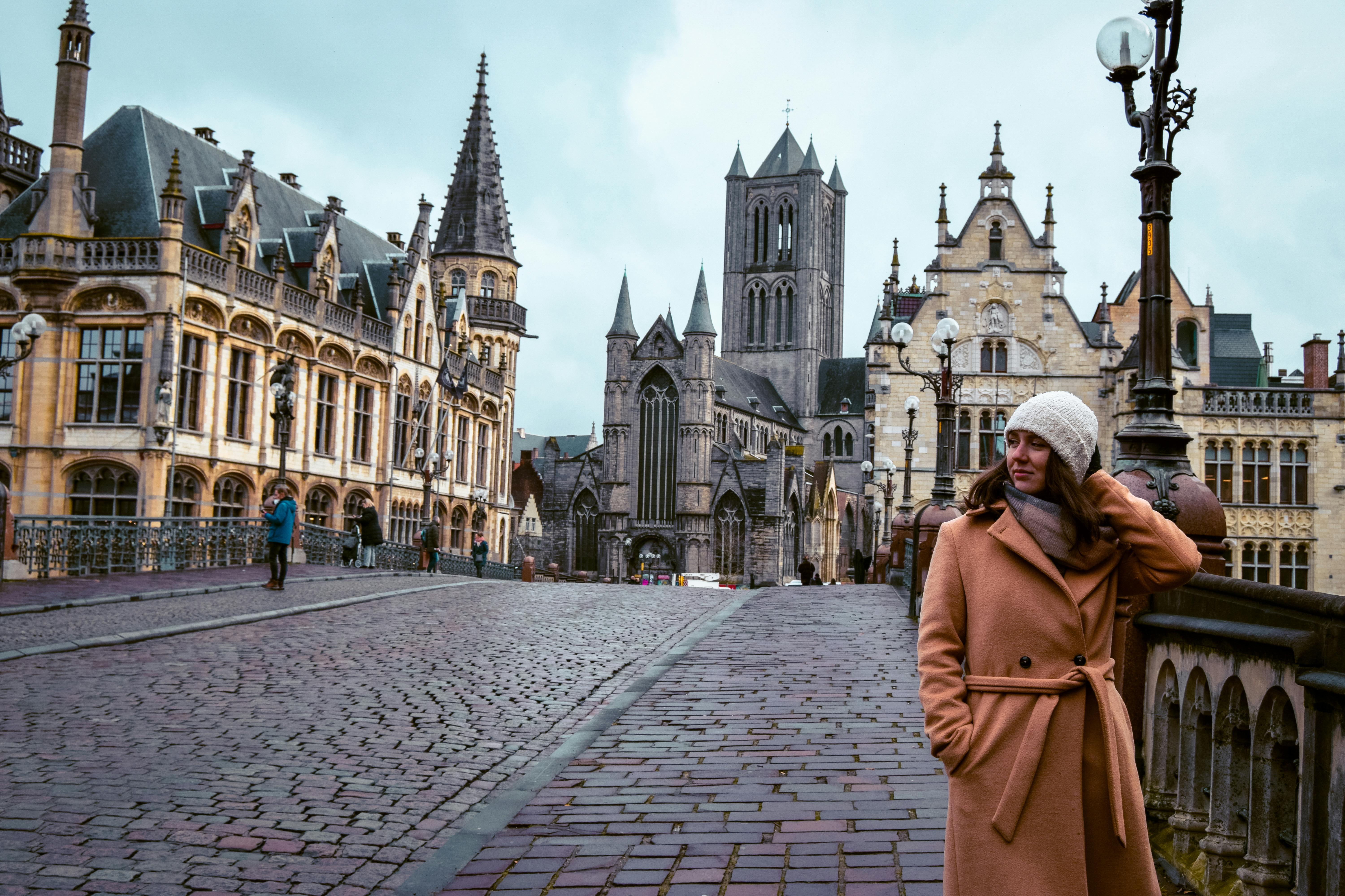 Woman in brown coat enjoys a winter day on a historic street in Ghent, Belgium.