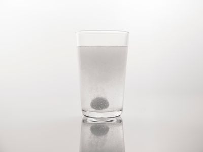 Effervescent tablet dissolving with bubbles in a clear glass of water