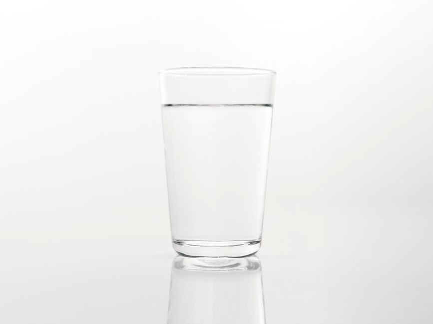 A simple close-up of a clear glass of water on a reflective white background.