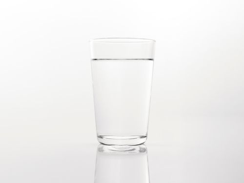 Free A simple close-up of a clear glass of water on a reflective white background. Stock Photo