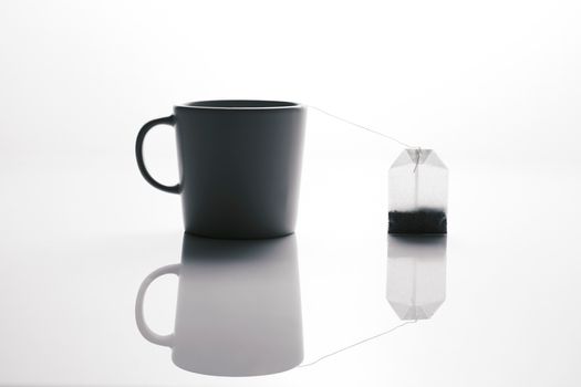 Elegant black mug with a tea bag, showcasing reflection in a minimalist style setting.