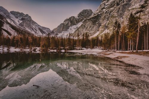 Free Panoramic view of a serene mountain lake with snow-covered peaks and pine forests during winter. Stock Photo