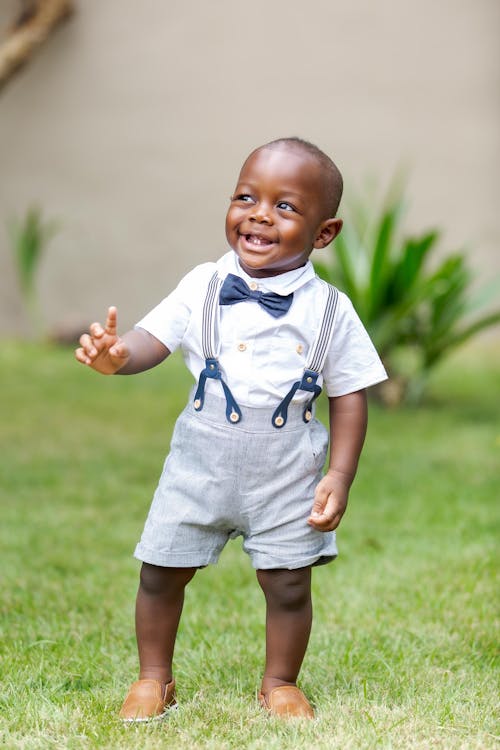 Boy in White Button Up Shirt and Gray Shorts Standing on Green Grass Field