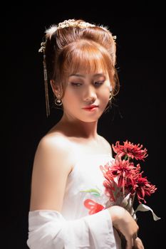 A beautiful woman in elegant attire holding red flowers, captured in a classic portrait style.