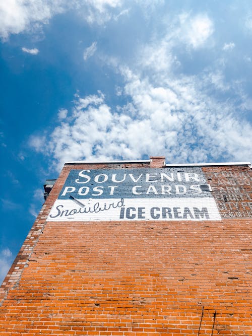 A Painted Signage on a Brick Wall Under Blue Sky  with White Clouds