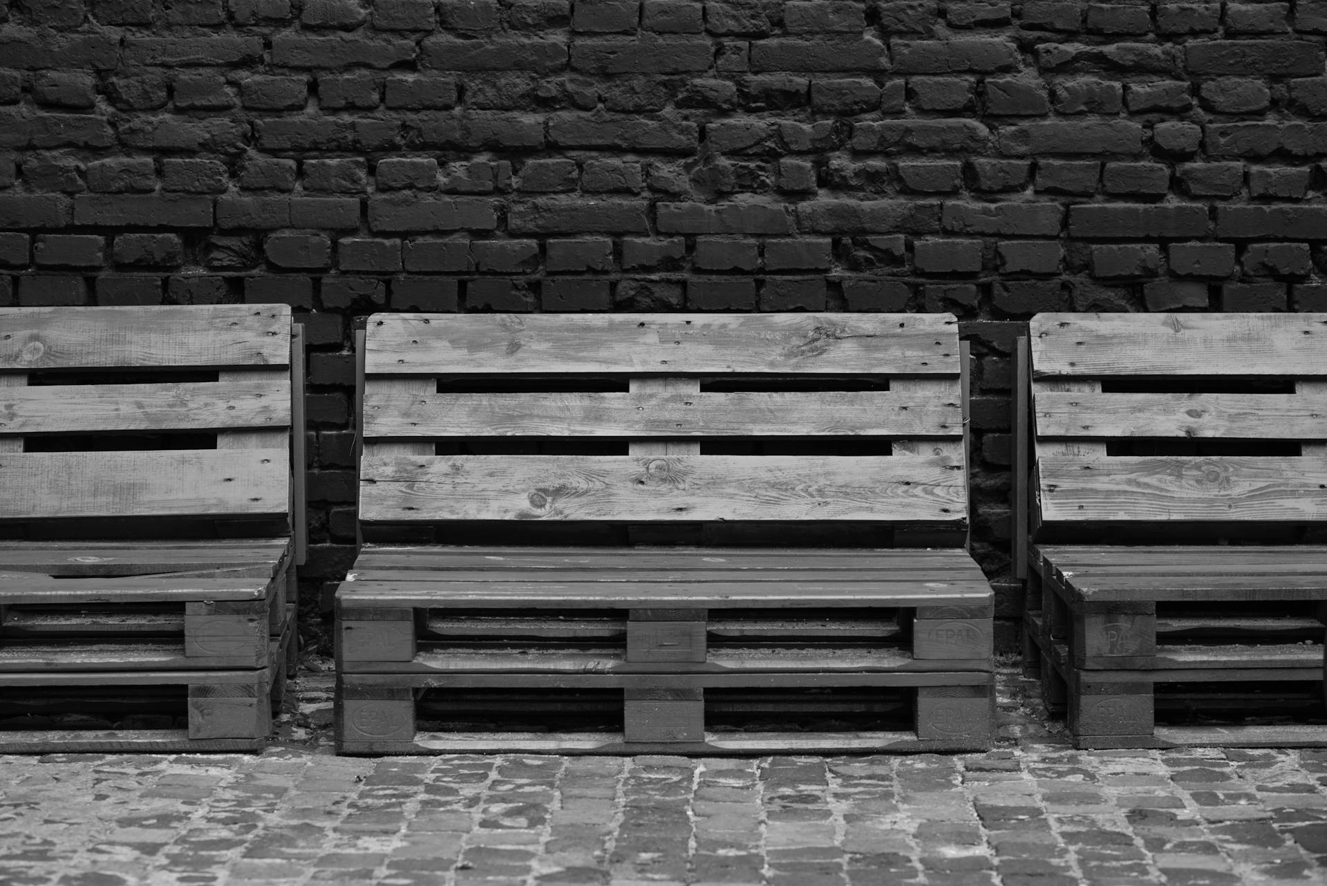 Black and white image of wooden pallet benches placed in front of a brick wall, showcasing minimalist design.