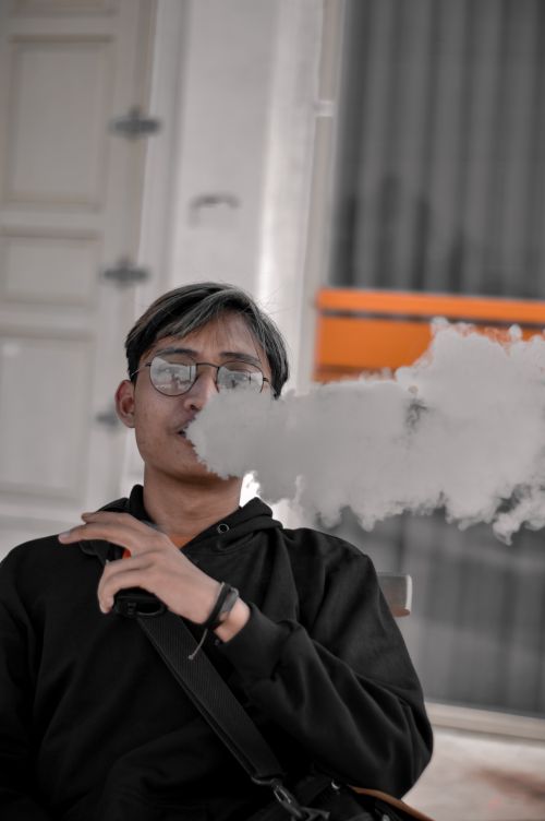Free Young man exhaling thick vapor while sitting, highlighting urban lifestyle habits. Stock Photo
