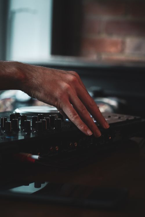 Free Close-up of a DJ's hand adjusting knobs on a mixer, creating music in a dimly lit indoor setting. Stock Photo