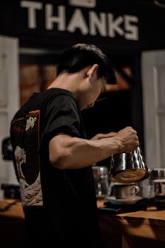 A barista carefully pours coffee using a kettle at a cozy indoor cafe.