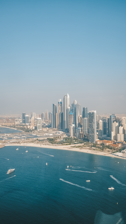 Free A captivating aerial shot showcasing Dubai's modern skyline along the waterfront with clear blue seas. Stock Photo
