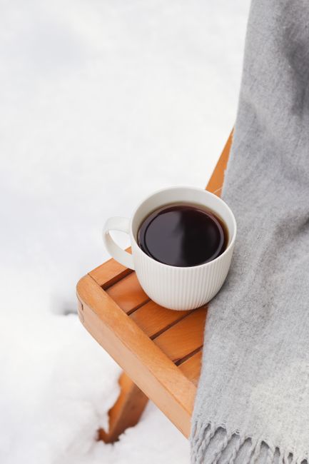 White coffee cup on a wooden table against a snowy backdrop, perfect for winter coziness.