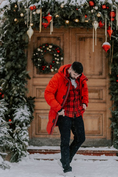 Free A Man Walking on Snow Covered Ground Near a Door Decorated with Christmas Decors Stock Photo