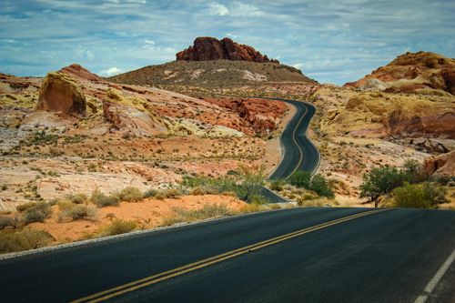 Free Scenic desert highway curving through vibrant sandstone hills under a cloudy sky. Stock Photo
