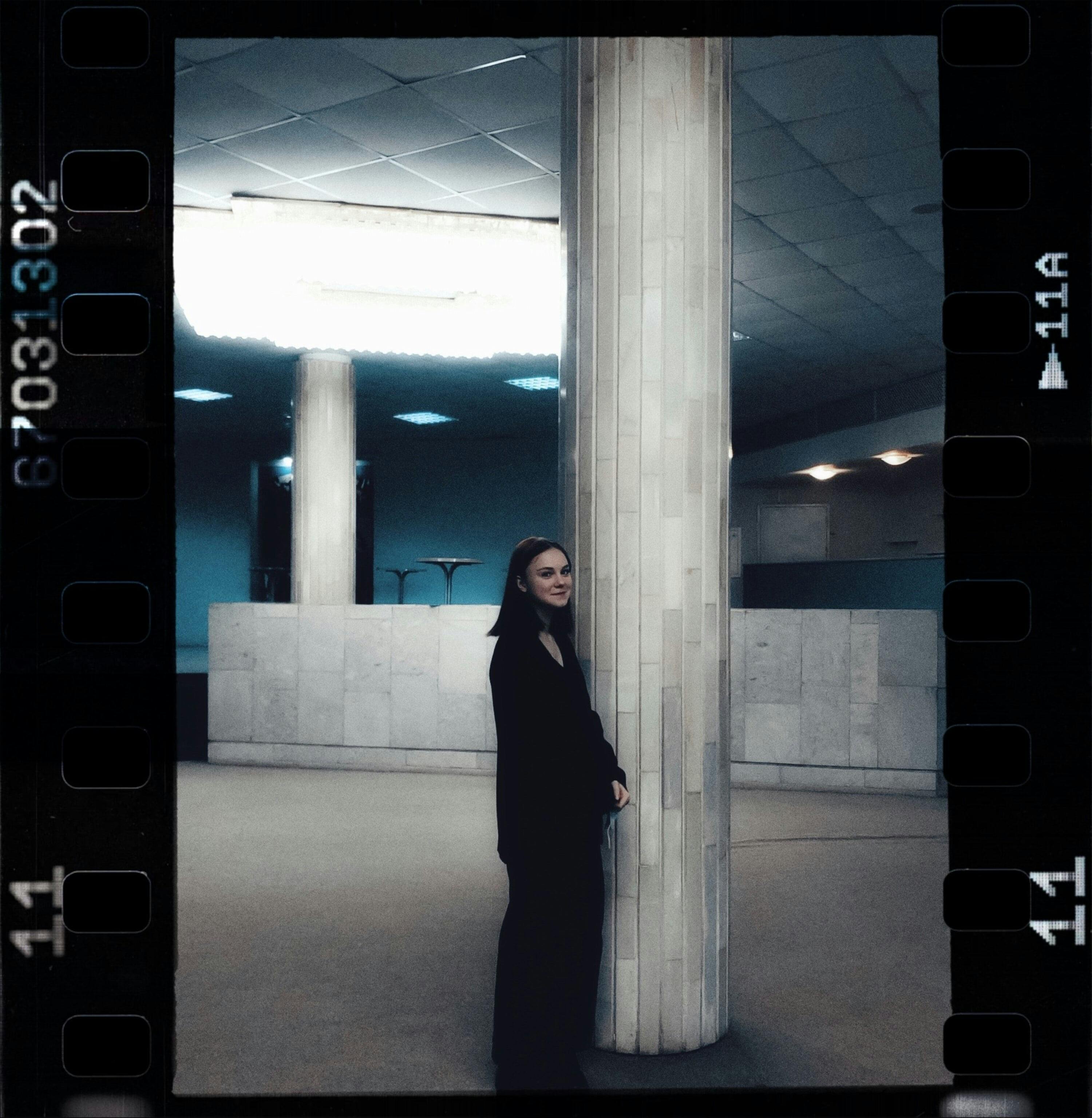 A stylish woman in a modern indoor setting, leaning against a column.