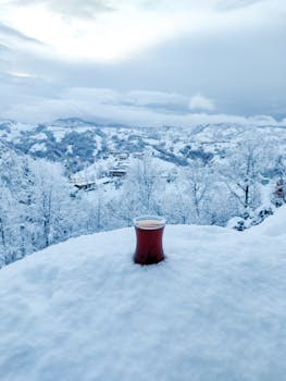 A steaming cup of tea on snow with a breathtaking winter mountain backdrop.