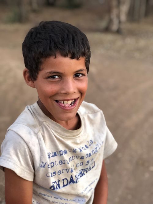 Free Portrait of a happy boy with a dirty shirt smiling outdoors in Moroccan setting. Stock Photo