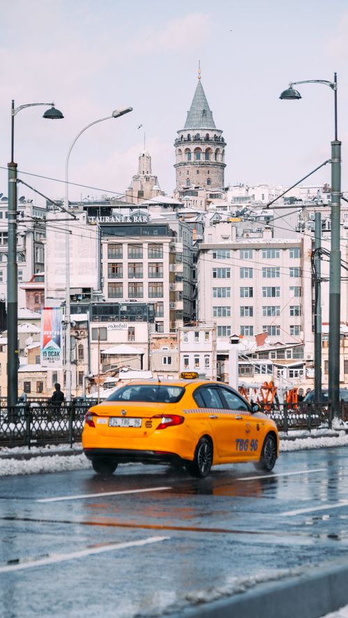 Free A city street scene featuring a yellow taxi in front of the historic Galata Tower in Istanbul's urban landscape. Stock Photo