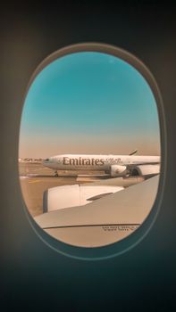 Photo of an Emirates airplane on the runway seen through an airplane window at Dubai Airport.