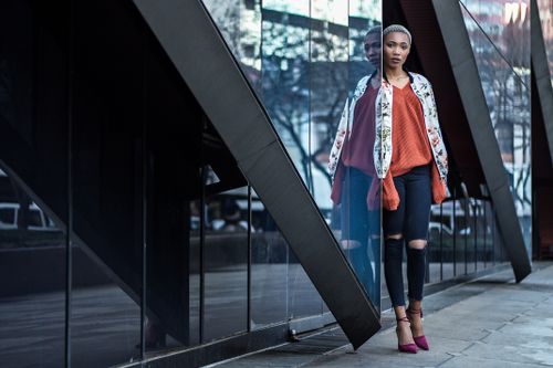 Free Woman in urban setting with glass facade reflecting, showcasing contemporary fashion. Stock Photo