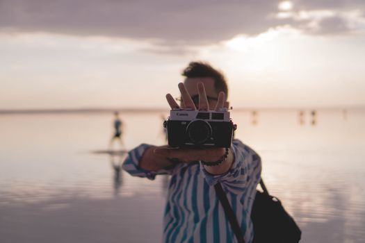 A man holding a vintage camera at sunset near a lake in Konya, Turkey.