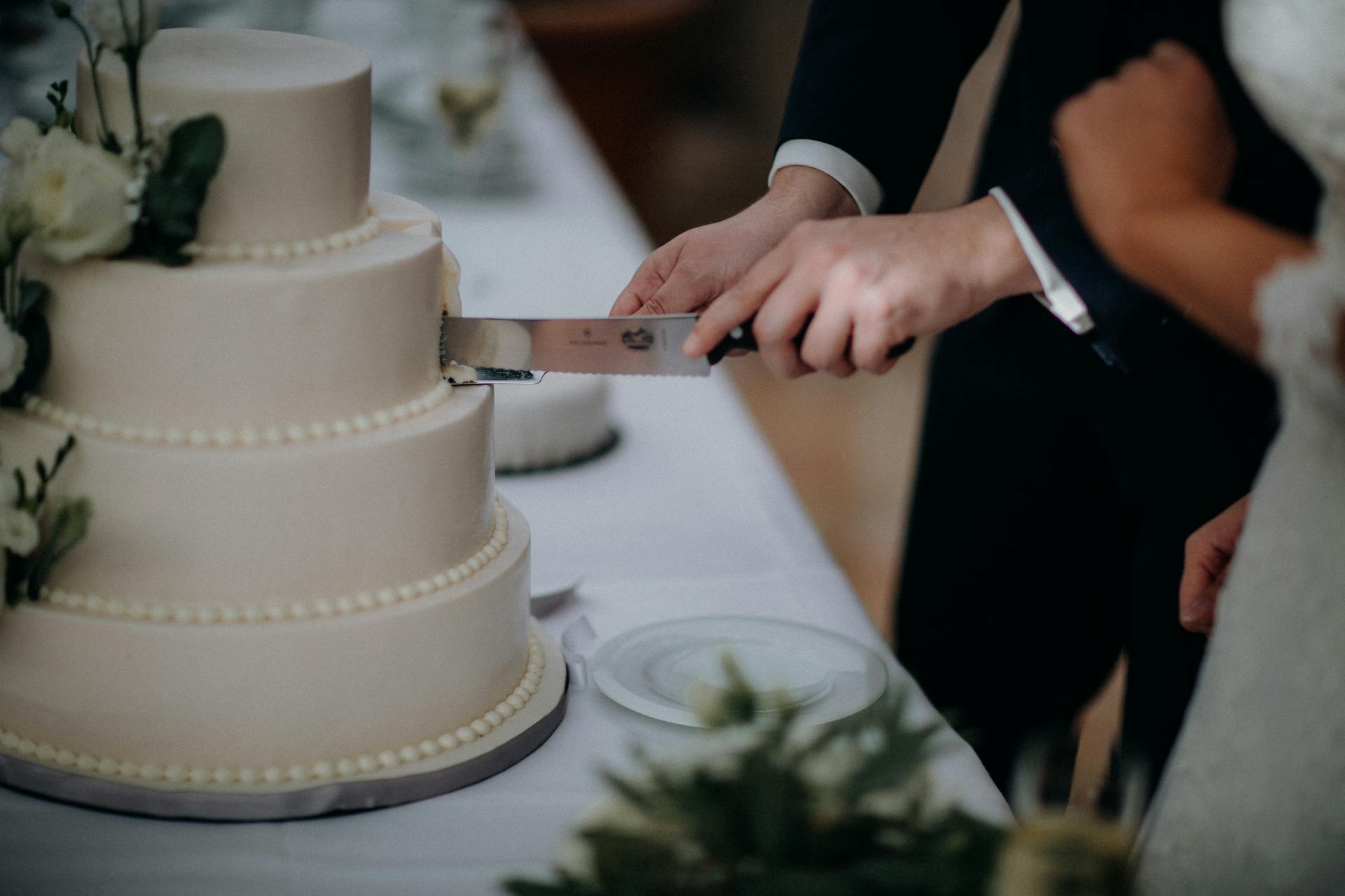 Close-up of a couple cutting a tiered wedding cake with flowers.