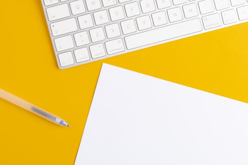 Close-Up Shot of a White Keyboard beside a Paper