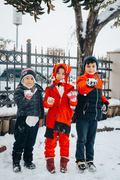 Free Three kids having fun in winter snow, wearing colorful outfits and making snowballs outdoors. Stock Photo