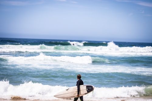 Free A surfer carrying a board walks towards the ocean at Boomerang Beach, NSW, capturing a perfect summer day. Stock Photo