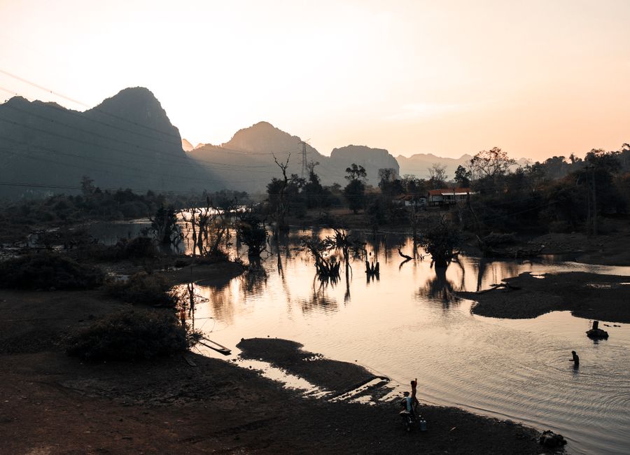 Peaceful sunset view of a lake with mountain backdrop in Laos, reflecting serene beauty and nature's tranquility.