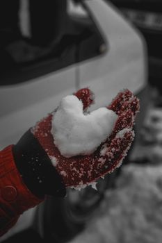 A heart-shaped snow piece in a red-gloved hand, outdoors in winter setting.