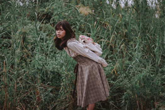 A young woman bending in lush greenery, exuding a serene and contemplative mood.