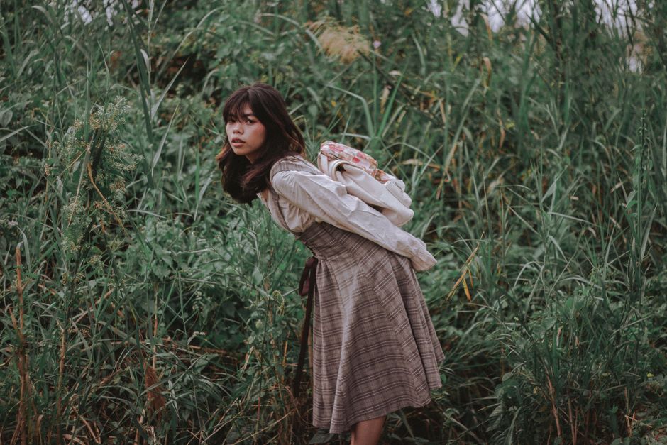 A young woman bending in lush greenery, exuding a serene and contemplative mood.