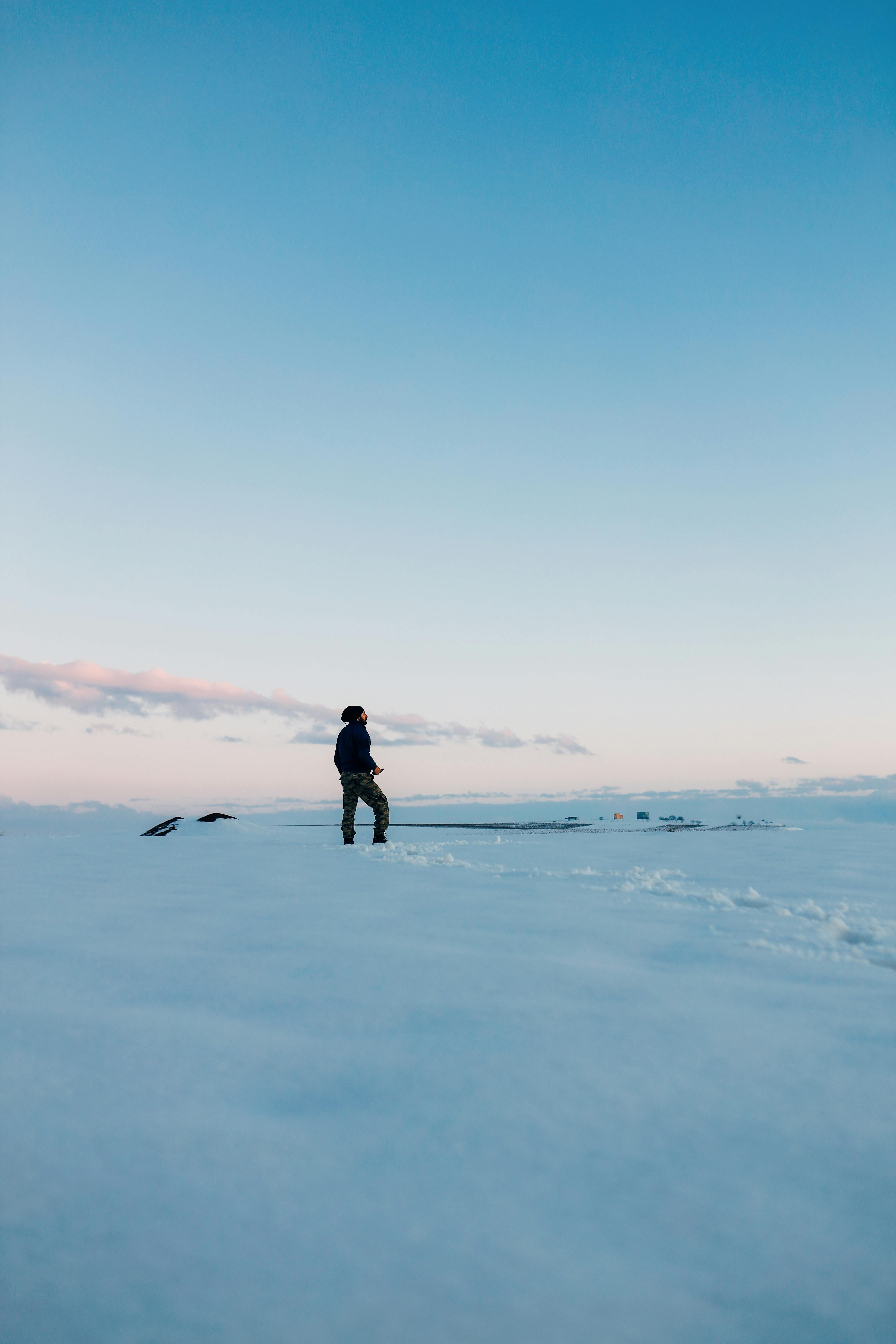 Silhouette of a person standing on a snow-covered field with a vibrant sunrise backdrop, symbolizing solitude and adventure.