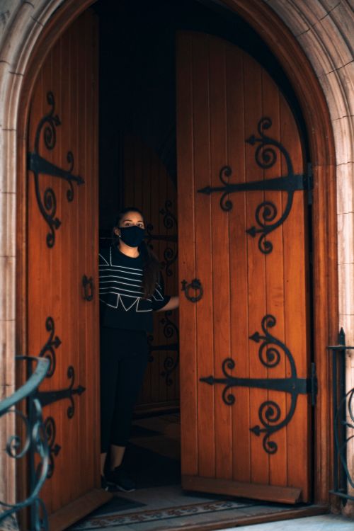 Free A woman wearing a face mask stands in an open wooden church doorway, symbolizing new normality. Stock Photo