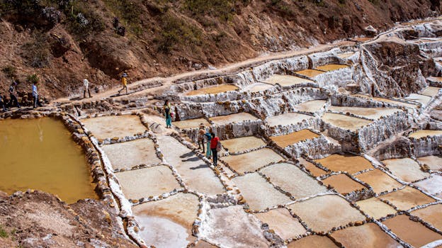 Tourists walk through the ancient salt ponds of Salinas de Maras in Peru during a sunny day.