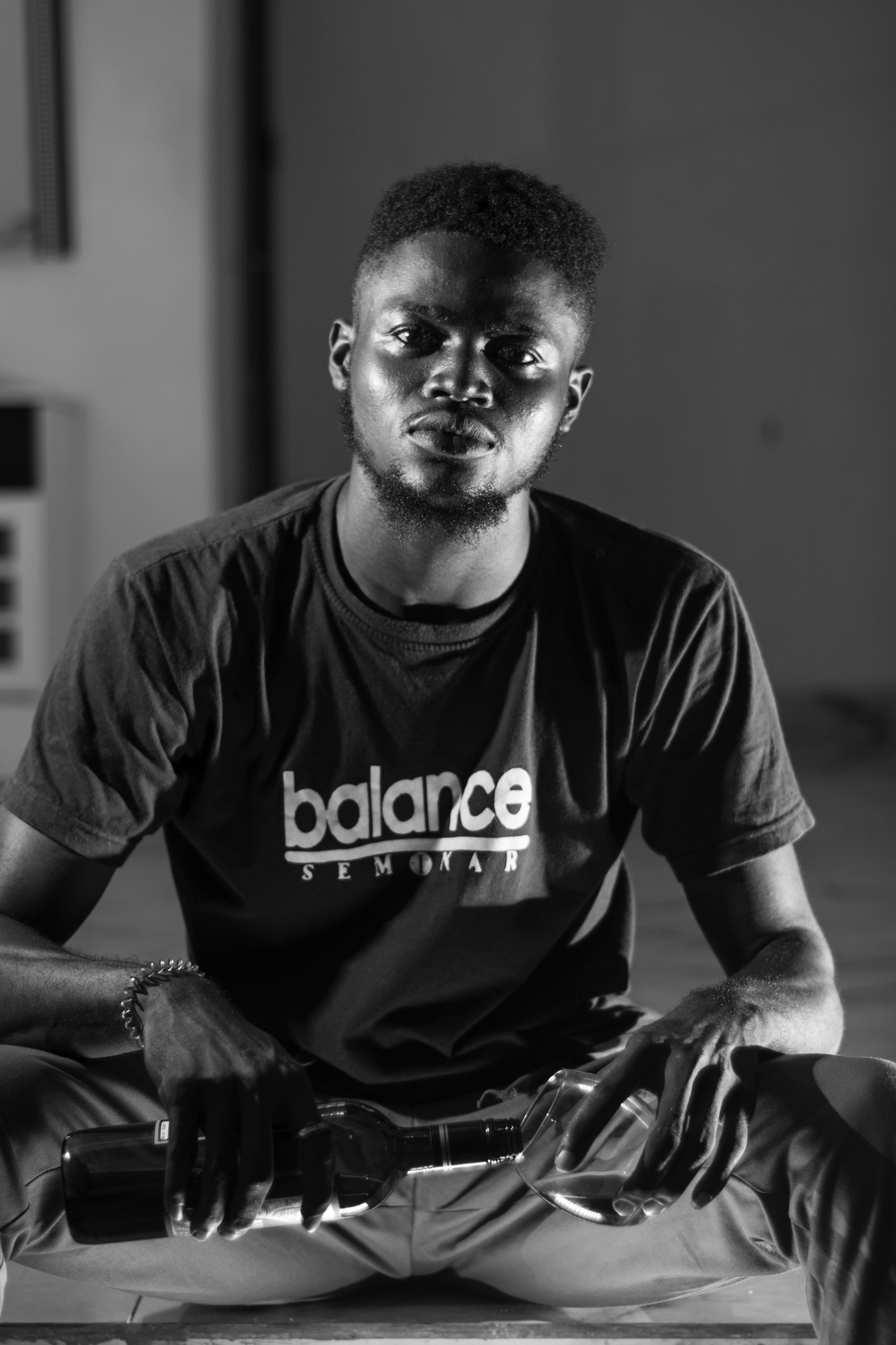 Young man in a black and white portrait holding a bottle indoors.