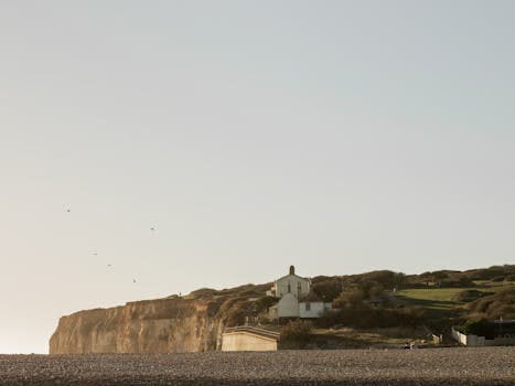 A serene coastal house atop a cliff in the English countryside, under a clear sky.